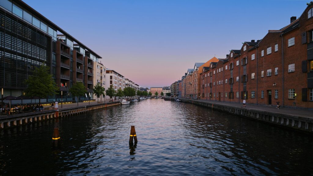 Peaceful canal in Copenhagen flanked by modern and historic buildings under a twilight sky.